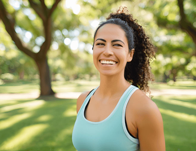 A woman stands in a lush park, taking a deep breath with a serene smile after a refreshing jog.